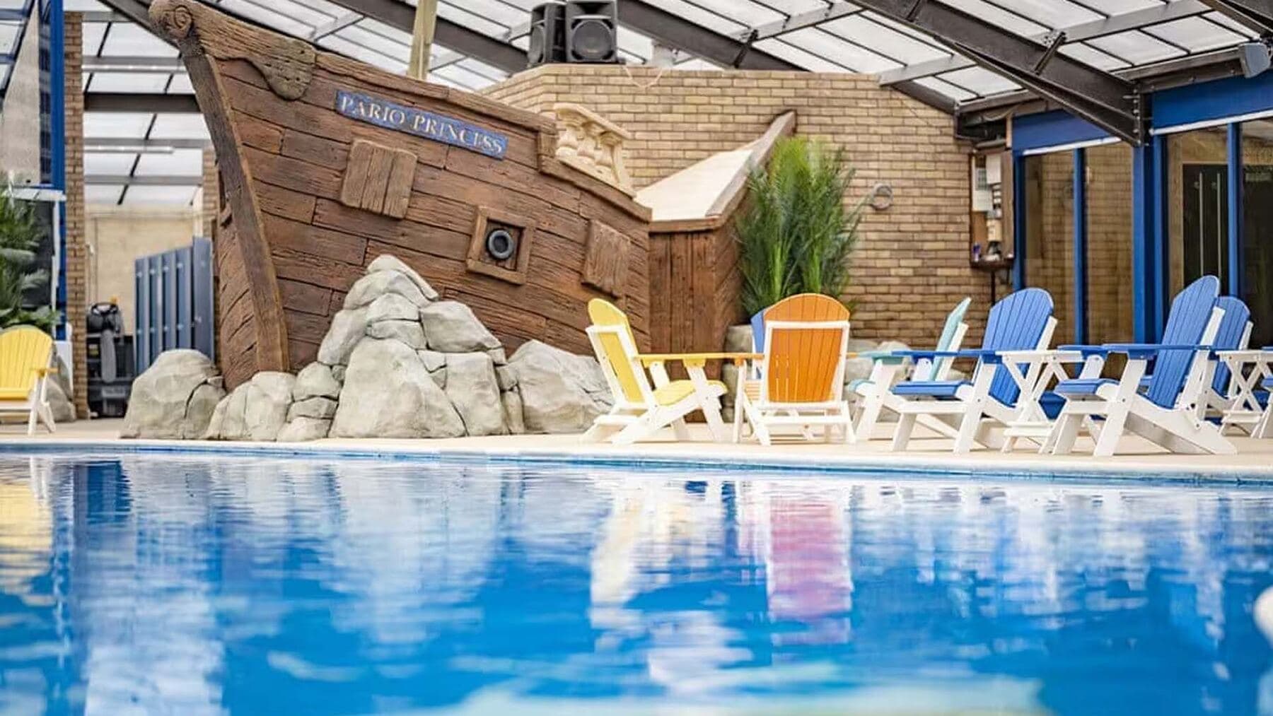 The holiday-park pool in the sunshine, deckchairs along the water beside the pirate-ship feature