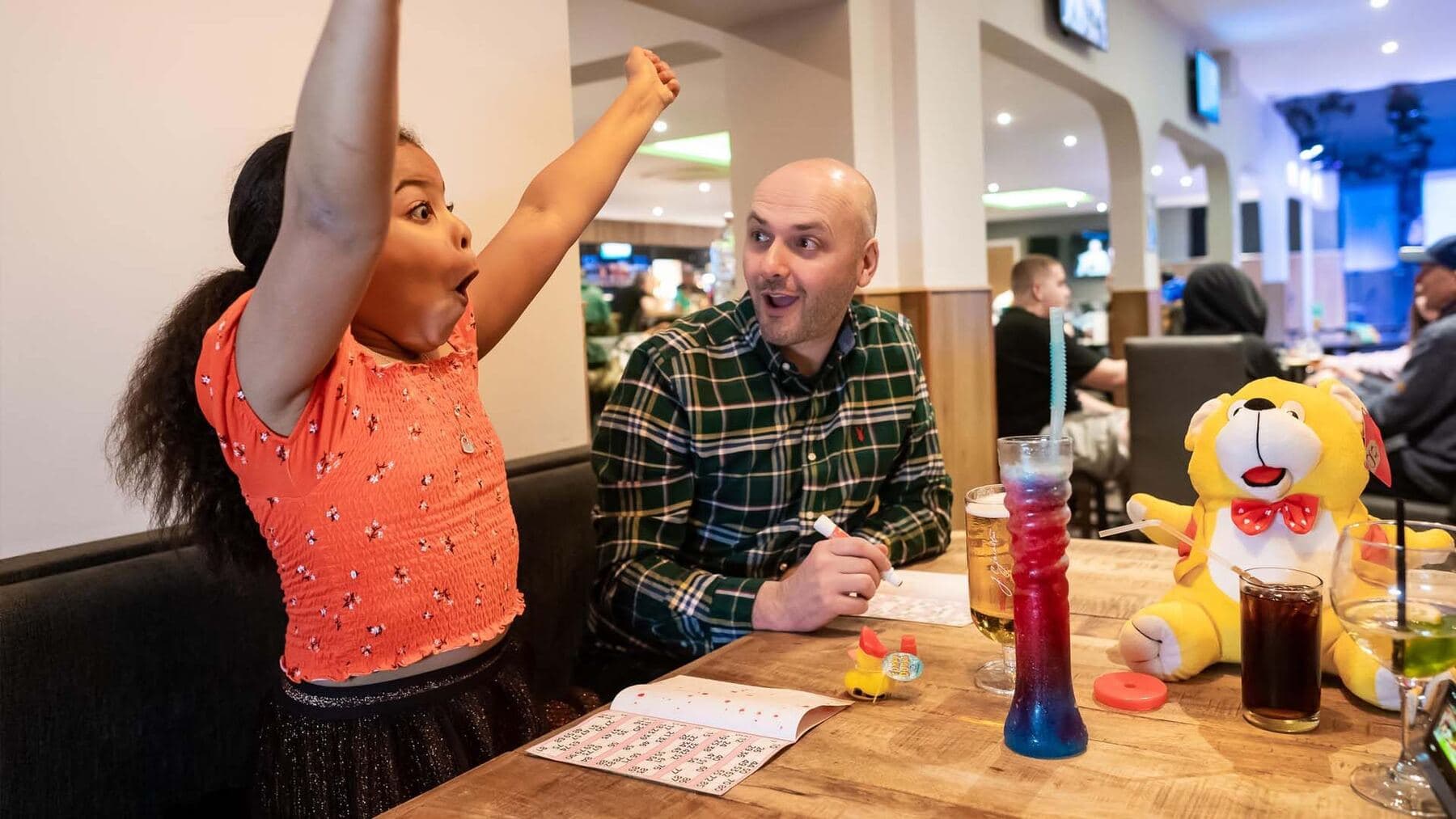 A girl cheering with her dad in the holiday-park arcade