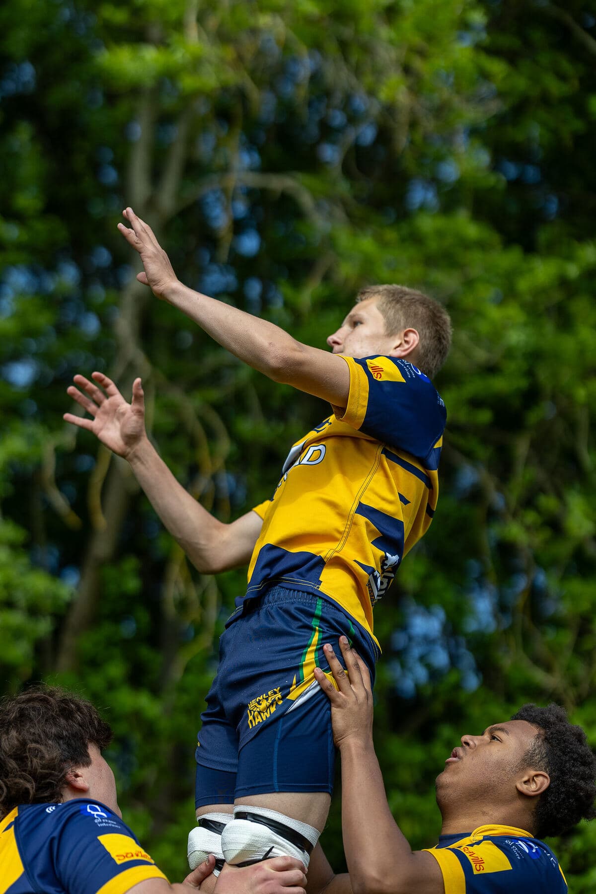 Two team-mates lifting a jumper high to take the ball at a lineout in bright sunshine