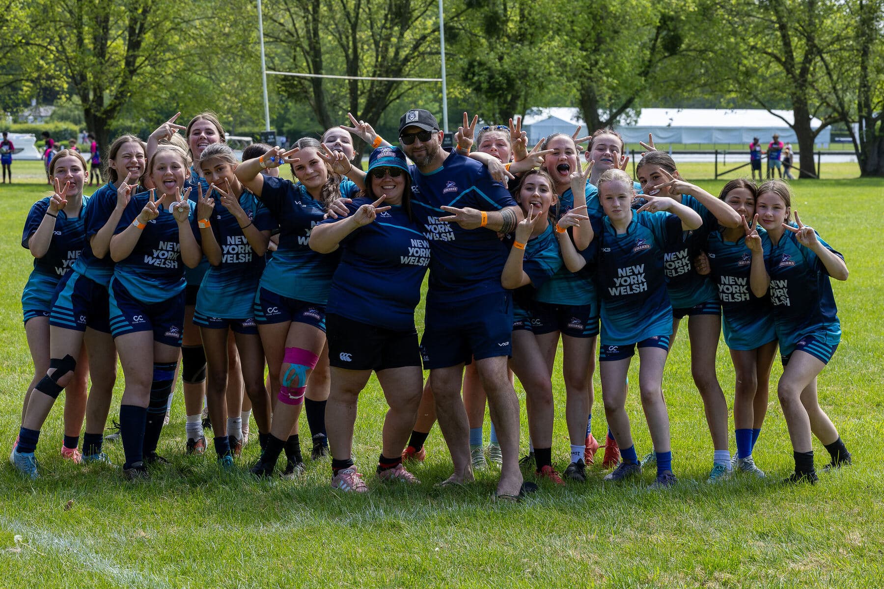 A girls squad in teal kit celebrating arm in arm on the pitch after their game