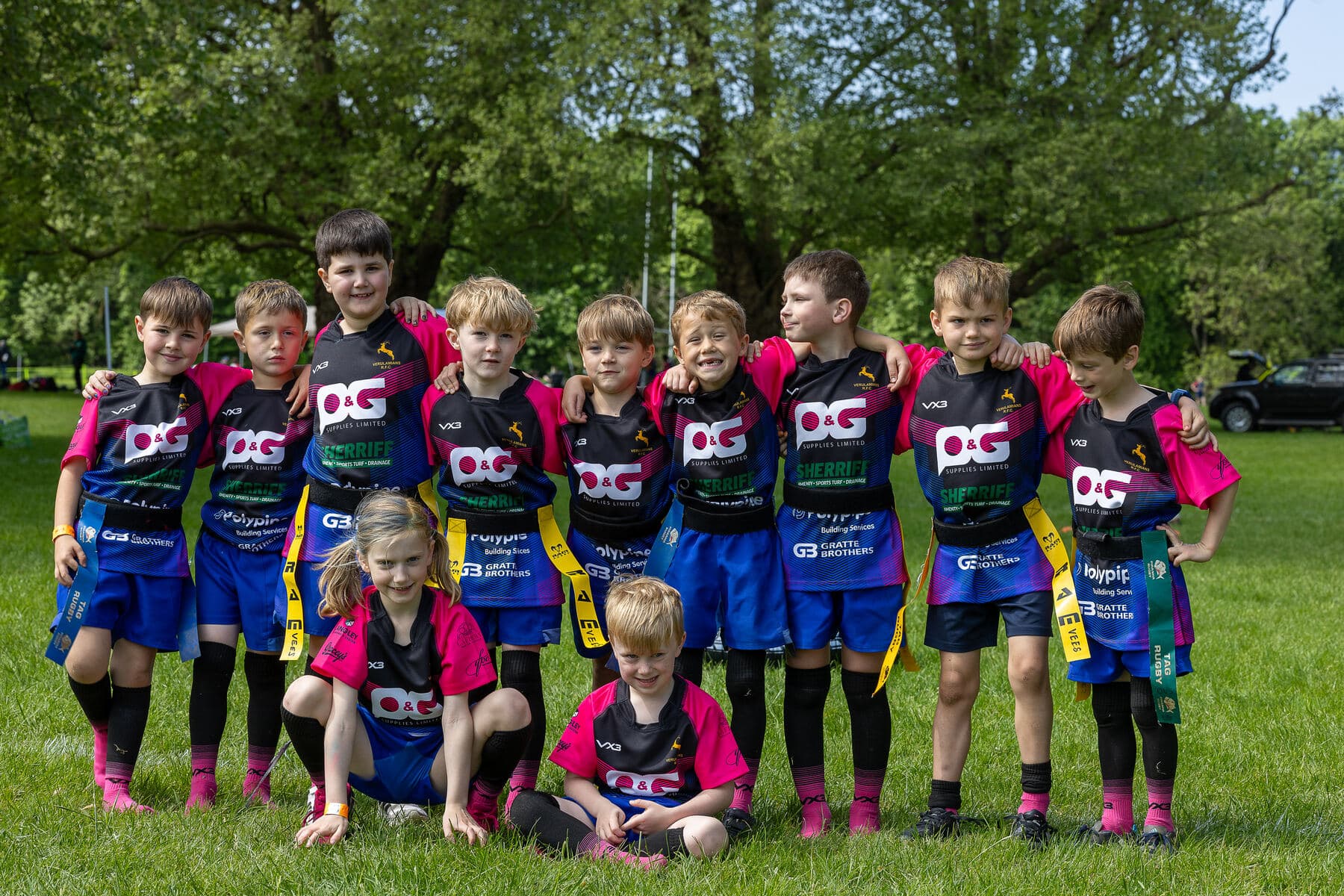 A touring team grouped together for a photograph under the trees beside the pitch