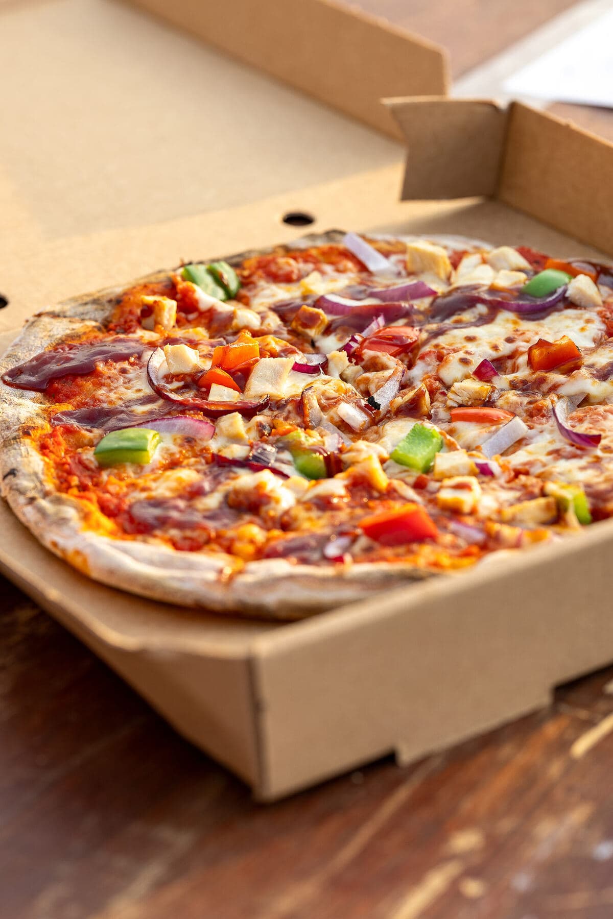A freshly delivered pizza in an open box on a wooden table