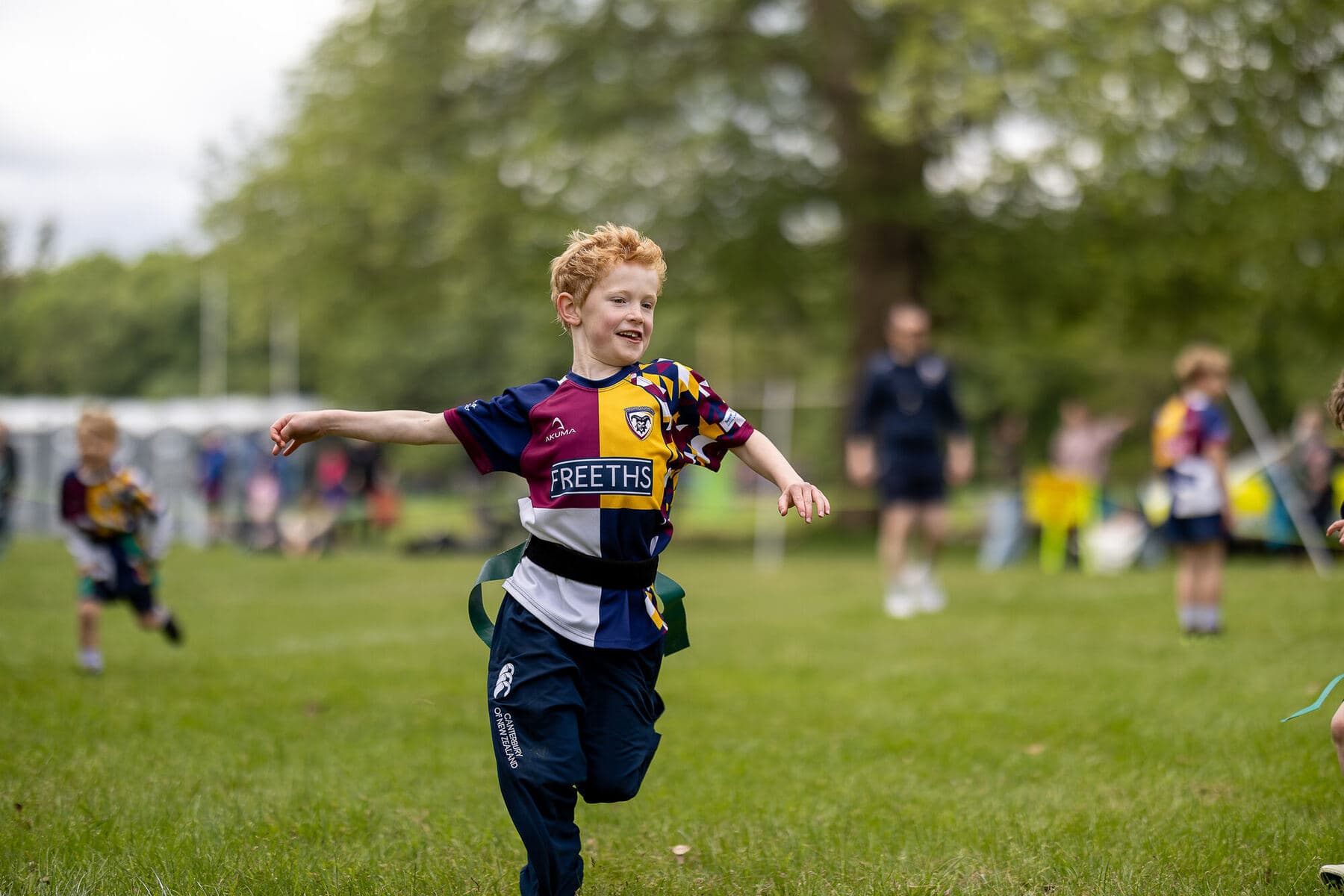 A young player in club kit running with the ball across a sunlit pitch, grinning