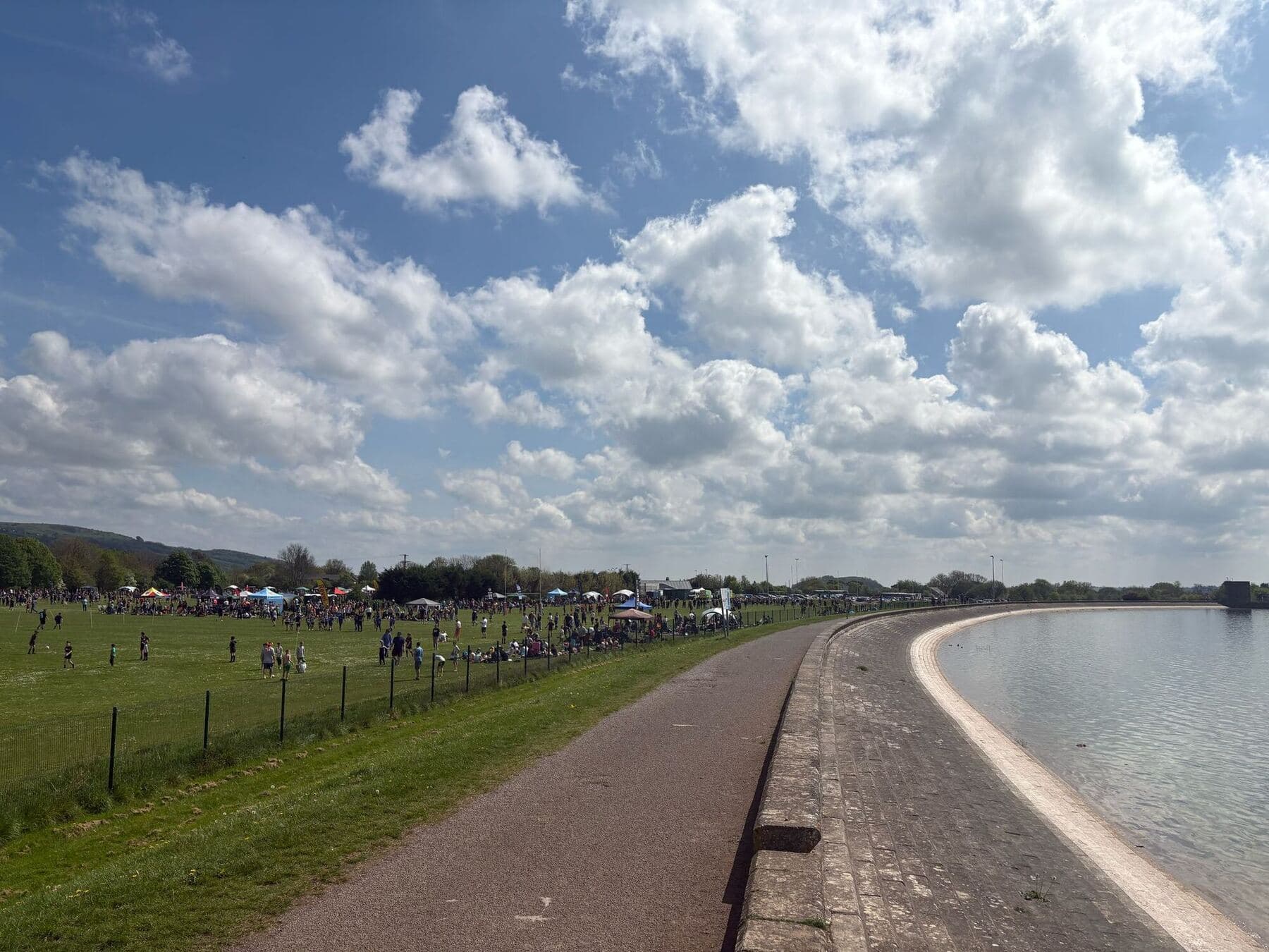 Festival pitches laid out along a lakeside path with hills behind