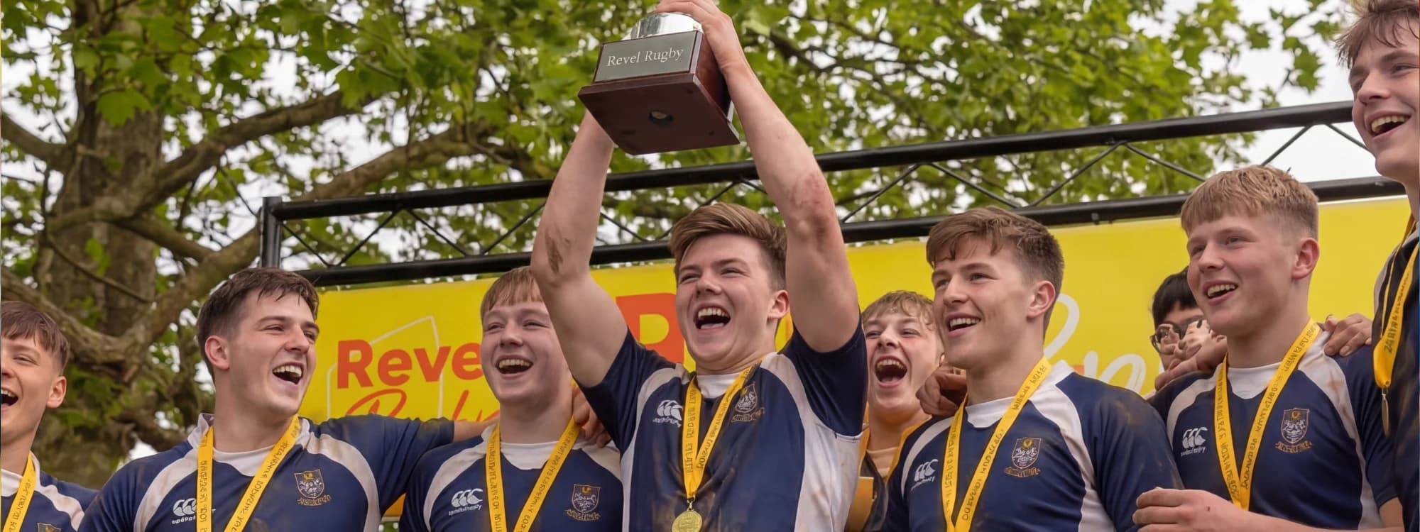 An older junior squad in navy and white roaring as their captain lifts the trophy above his head