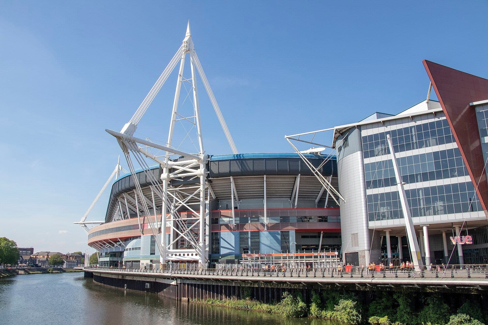 The Principality Stadium and its masts beside the River Taff under a blue sky